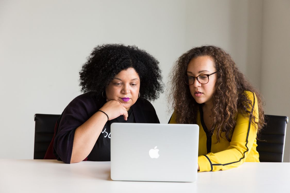 Two women seated together reviewing a laptop screen.